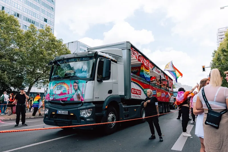 Paradetruck mit Regenbogenfahnen und Publikum am Straßenrand